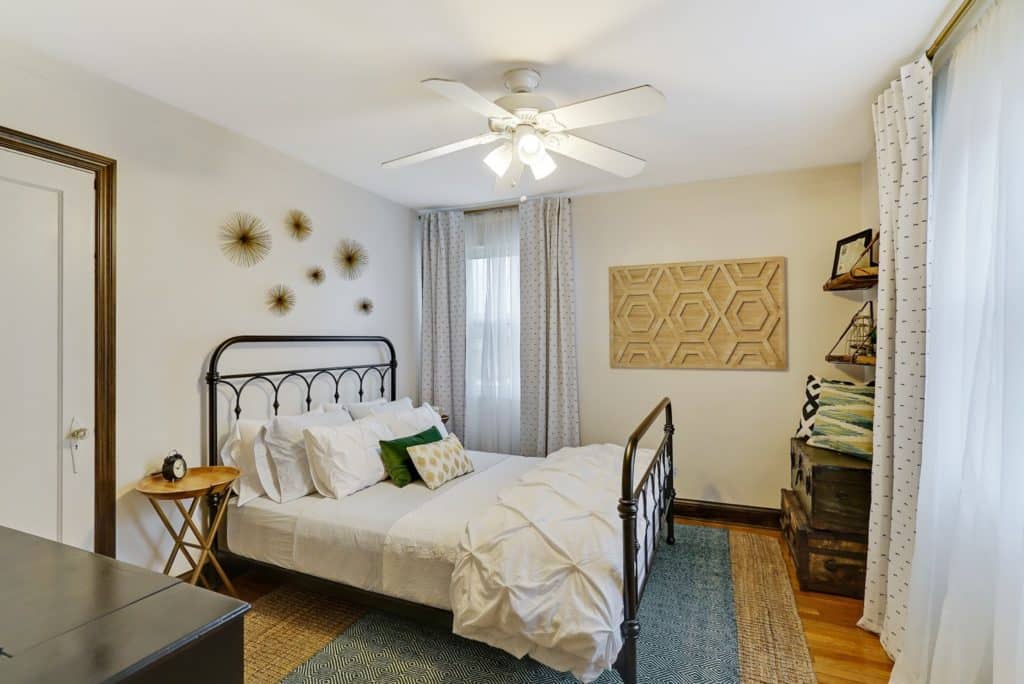 Wrought iron bed with white bedding on a sisal rug and white walls.