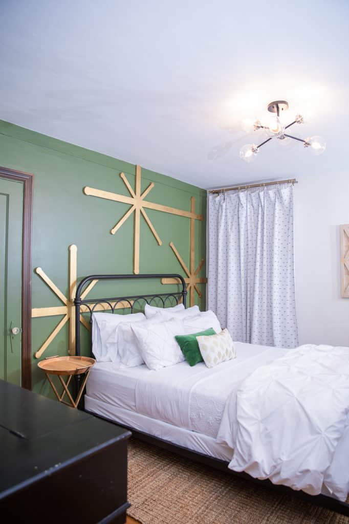 Green walls with giant gold stars and a wrought iron bed with white bedding on a sisal rug.