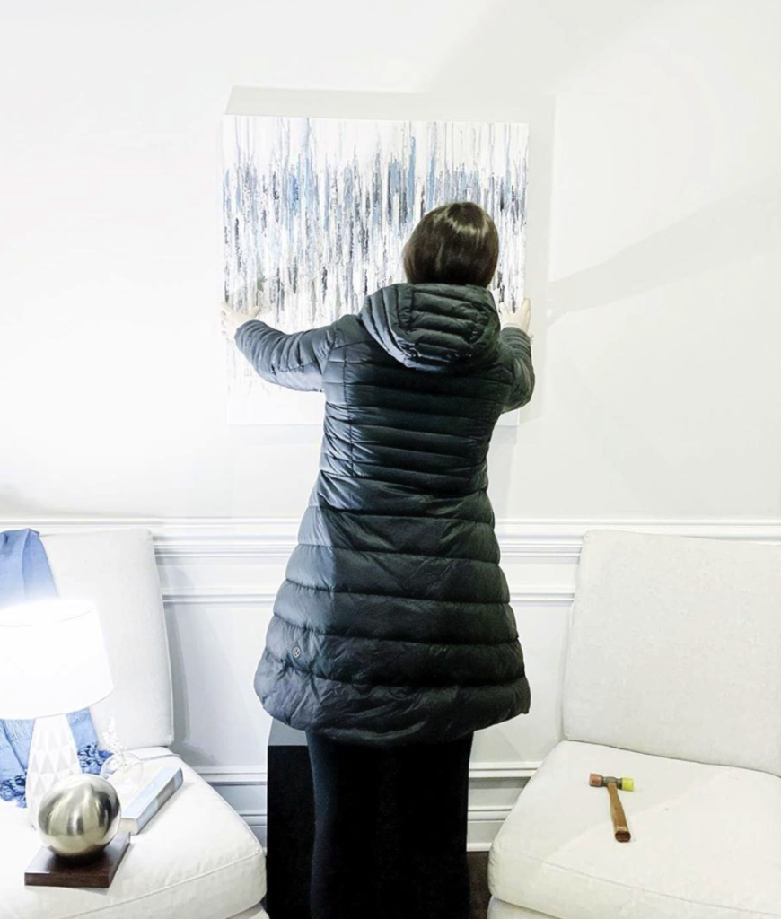 A woman hanging a piece of art in her home