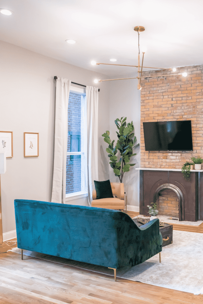 A living room with a blue-green couch, brick fireplace, and flat-screen TV.