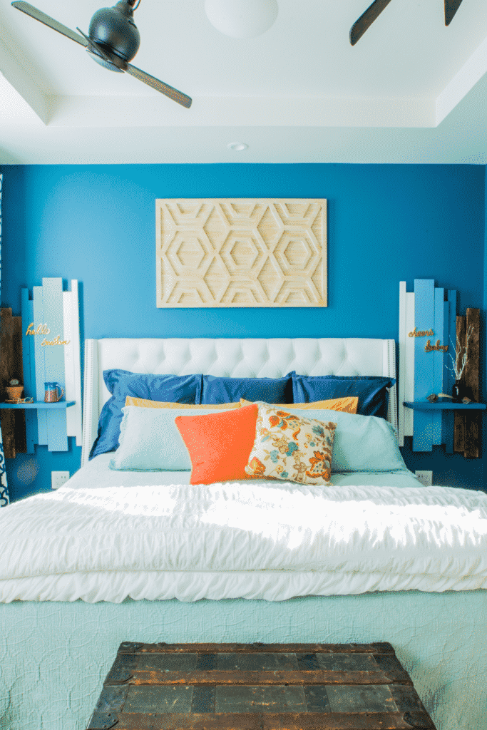 A blue painted bedroom with a colorful bed and an old, wooden chest. 