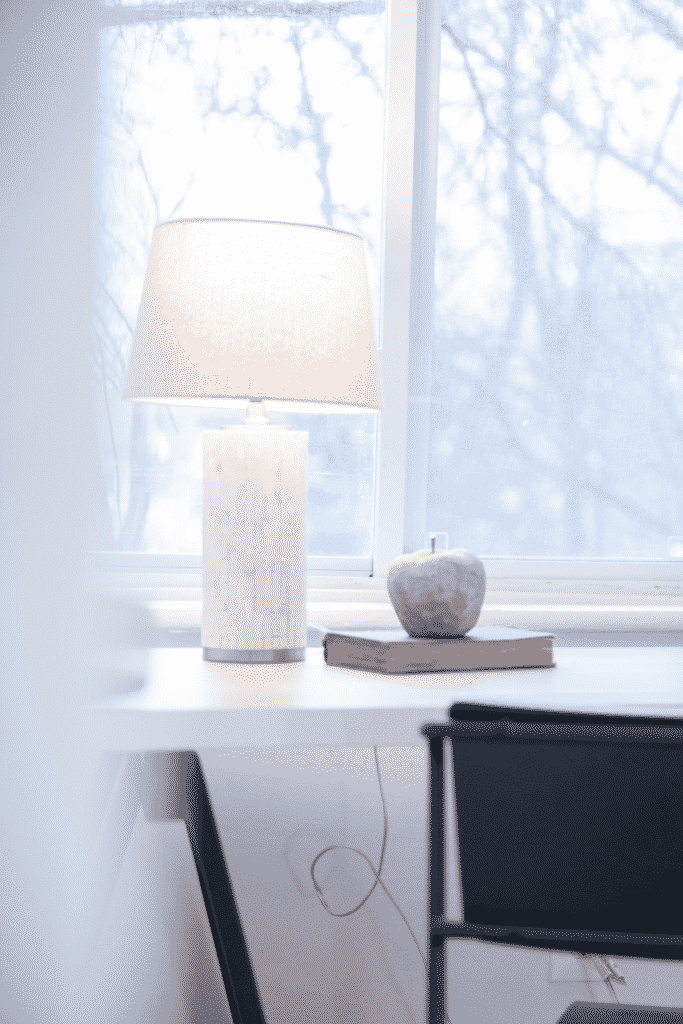 A desk, chair, and white lamp in front of a large window.