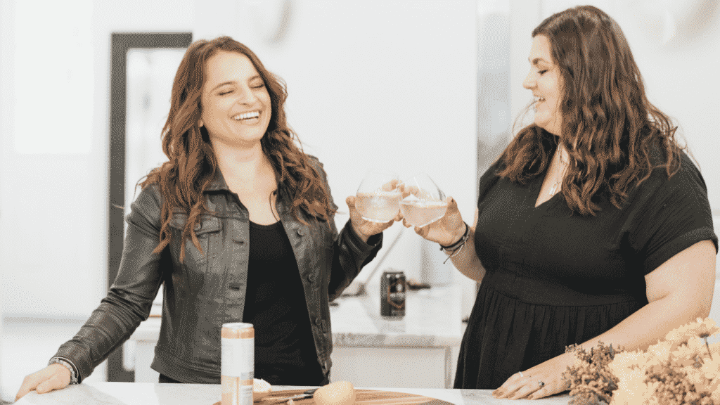 Two women happily sharing glasses of wine in a kitchen