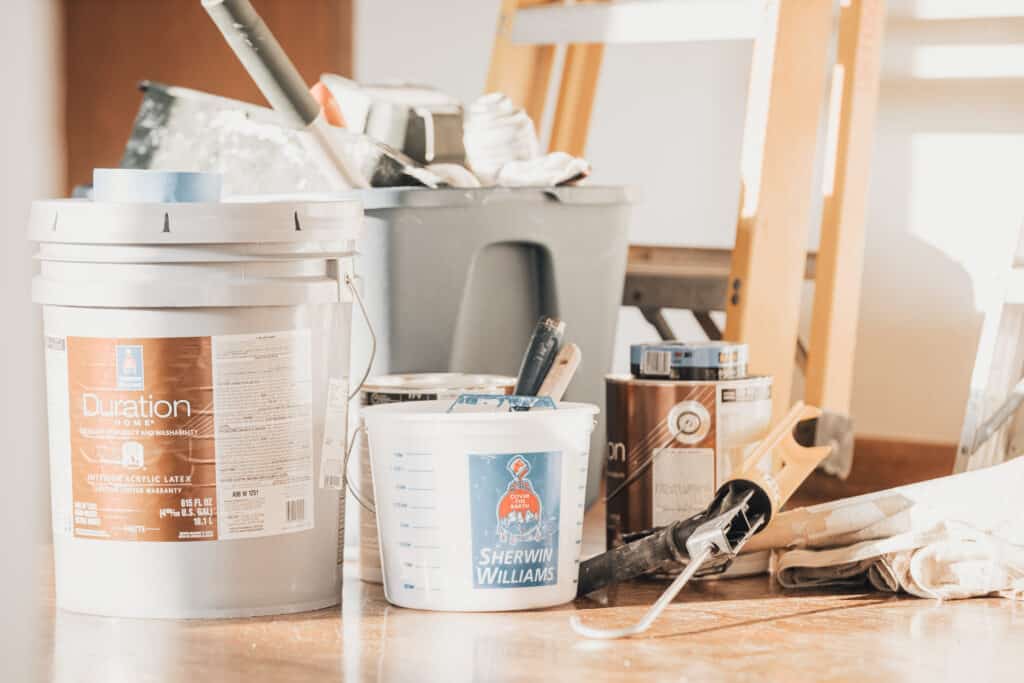 Paint cans, brushes, and a roller filled with brown paint for a wall touch up.